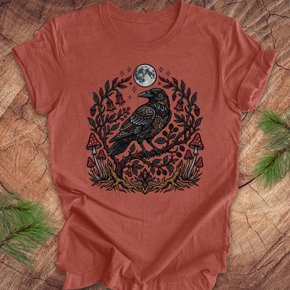 Clay colored t-shirt with a raven and nature-themed design on a wooden surface.