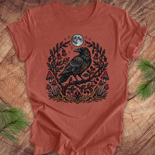 Clay colored t-shirt with a raven and nature-themed design on a wooden surface.