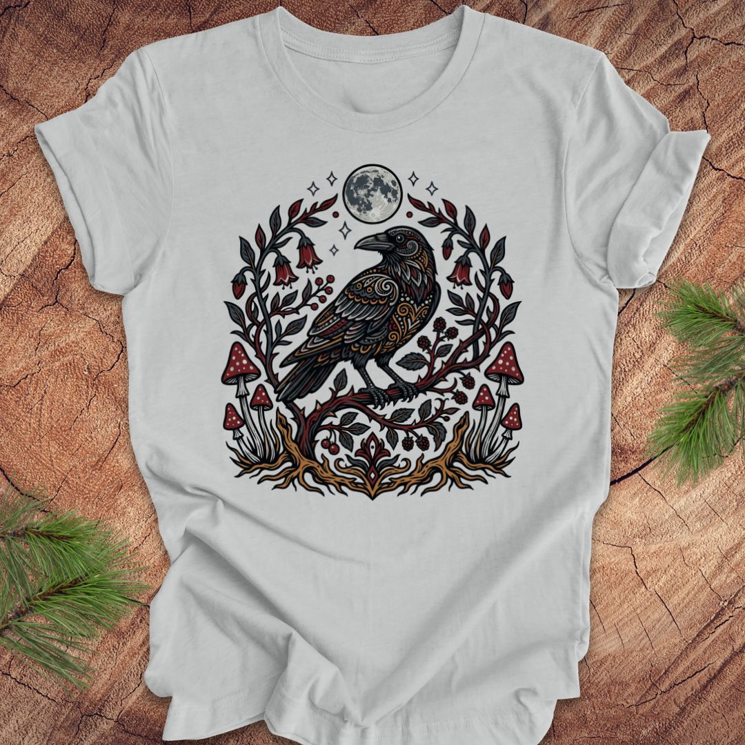 Gray t-shirt with a raven and nature-themed design on a wooden surface.