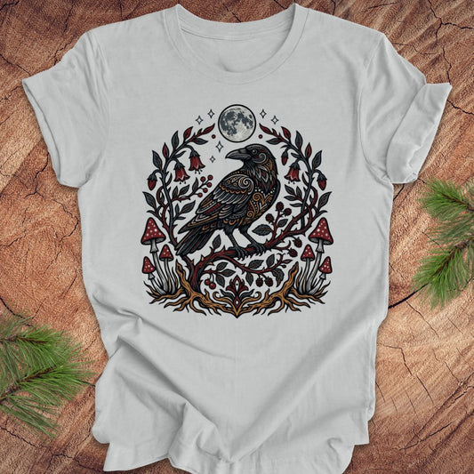 Gray t-shirt with a raven and nature-themed design on a wooden surface.