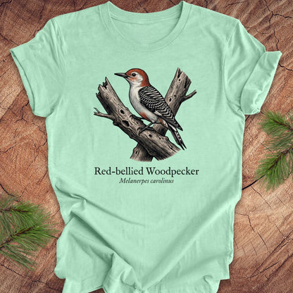 Light green t-shirt with a red-bellied woodpecker graphic and text on a wooden surface.