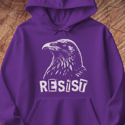 A purple pullover hoodie with a white graphic of a raven and the word 'RESIST' printed on the front, displayed against a rustic wood background.