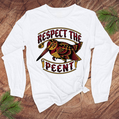 White long-sleeve shirt with a graphic design of a woodcock and text 'Respect the Peent' on a wooden surface.