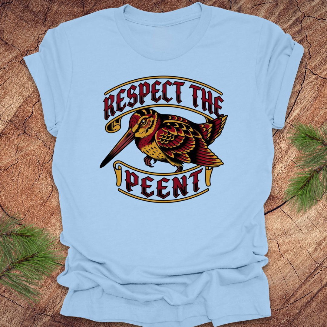 Light blue t-shirt with a graphic design of a bird and text 'Respect the Peent' on a wooden surface.