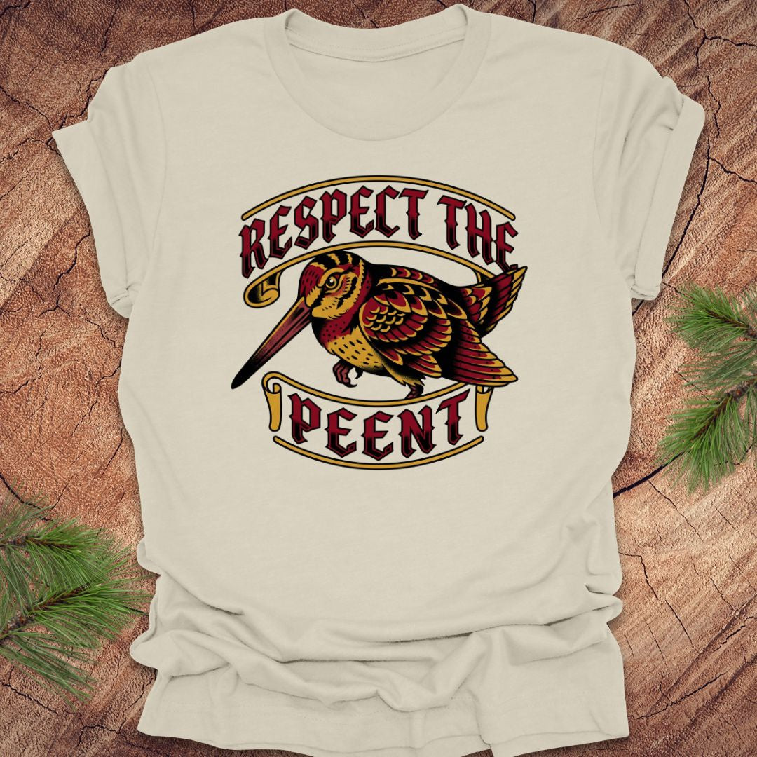 Beige t-shirt with a graphic design of a bird and text 'Respect the Peent' on a wooden surface.