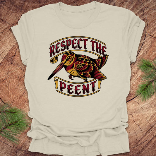 Beige t-shirt with a graphic design of a bird and text 'Respect the Peent' on a wooden surface.