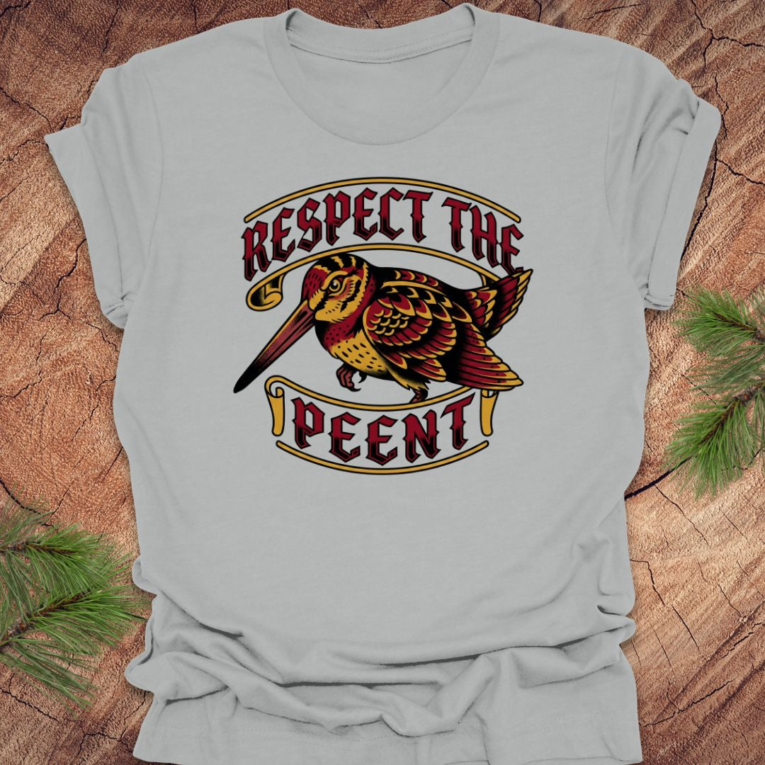 Gray t-shirt with a graphic design of a bird and text 'Respect the Peent' on a wooden surface.
