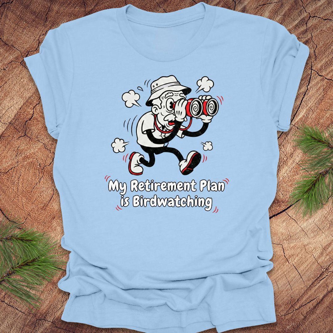 Light blue t-shirt with a cartoon character and text 'My Retirement Plan is Birdwatching' on a wooden surface.