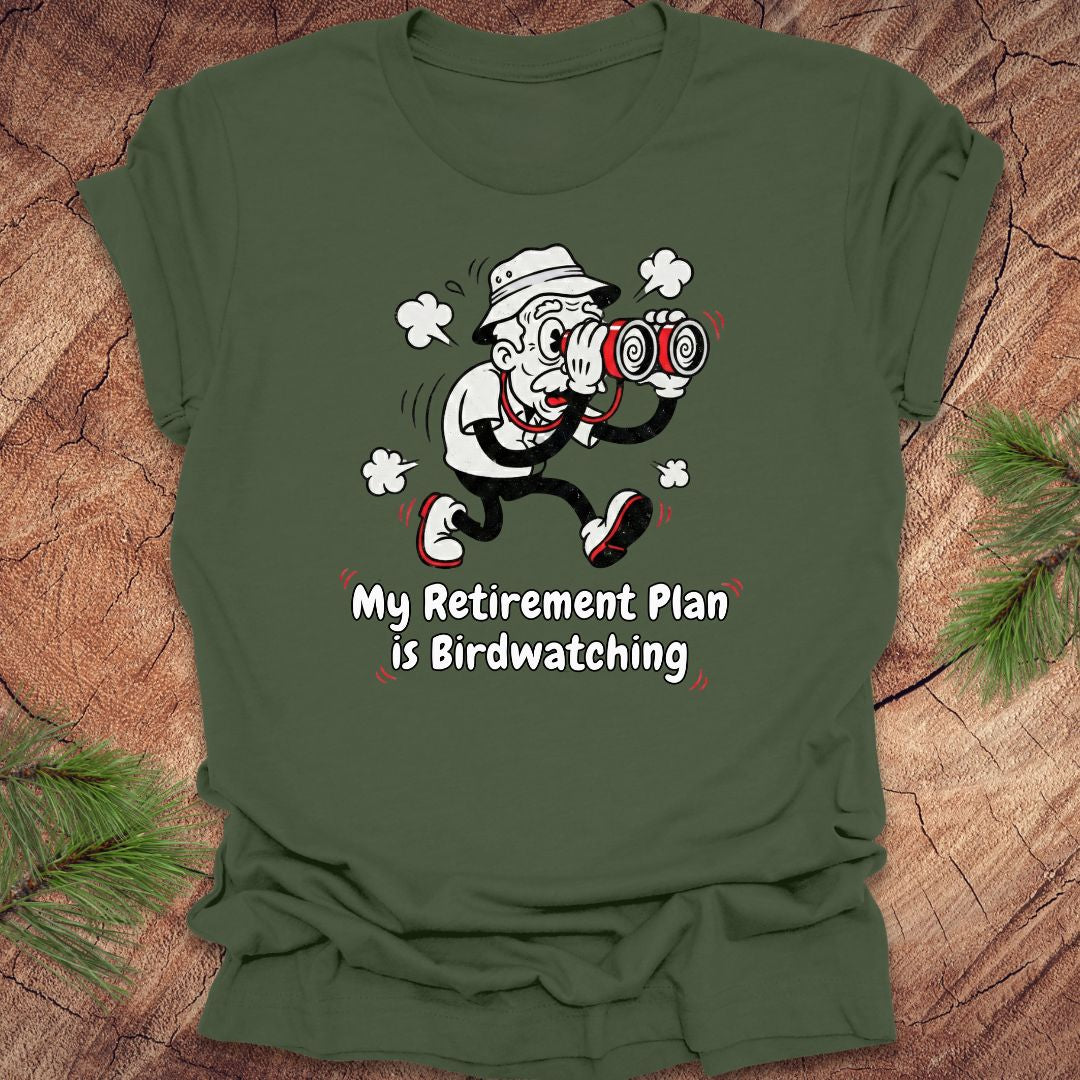 Green t-shirt with a cartoon character and text 'My Retirement Plan is Birdwatching' on a wooden surface.