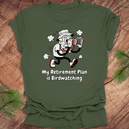 Green t-shirt with a cartoon character and text 'My Retirement Plan is Birdwatching' on a wooden surface.