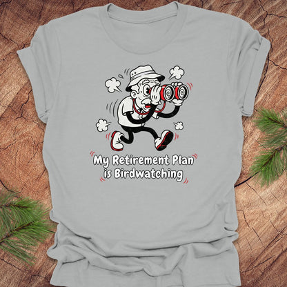 Gray t-shirt with a cartoon character and text 'My Retirement Plan is Birdwatching' on a wooden surface.