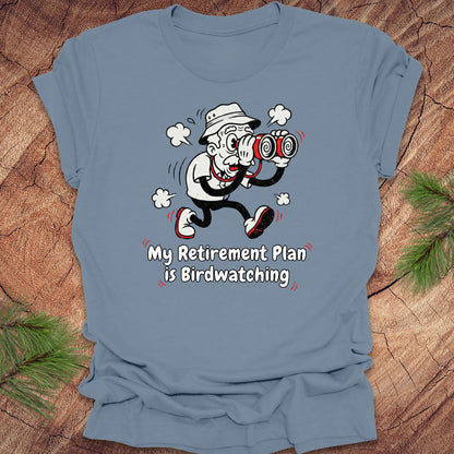 Blue t-shirt with a cartoon character and text 'My Retirement Plan is Birdwatching' on a wooden surface.