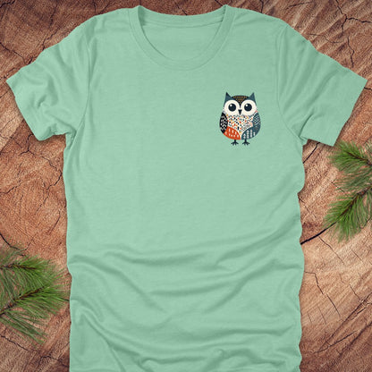 Light green t-shirt with a pocket owl design on a wooden surface