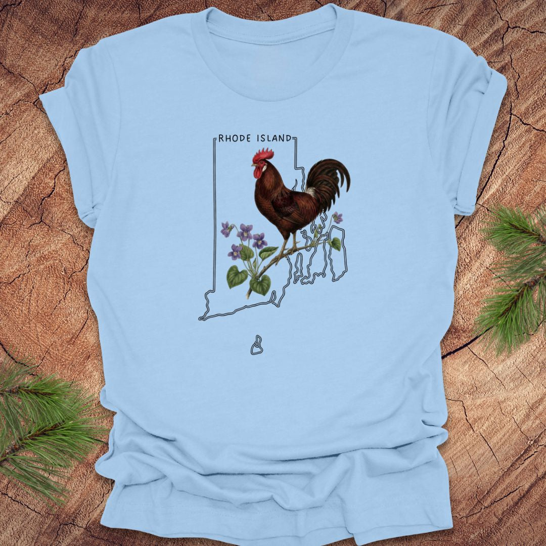 Baby blue t-shirt with the state outline of Rhode Island with state bird, red rooster and flower, violet,  on a wooden surface