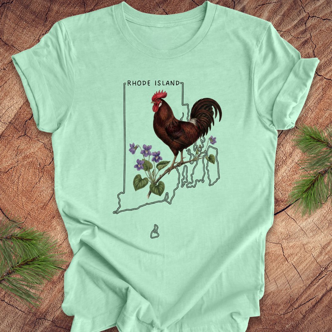 Mint green t-shirt with the state outline of Rhode Island with state bird, red rooster and flower, violet,  on a wooden surface