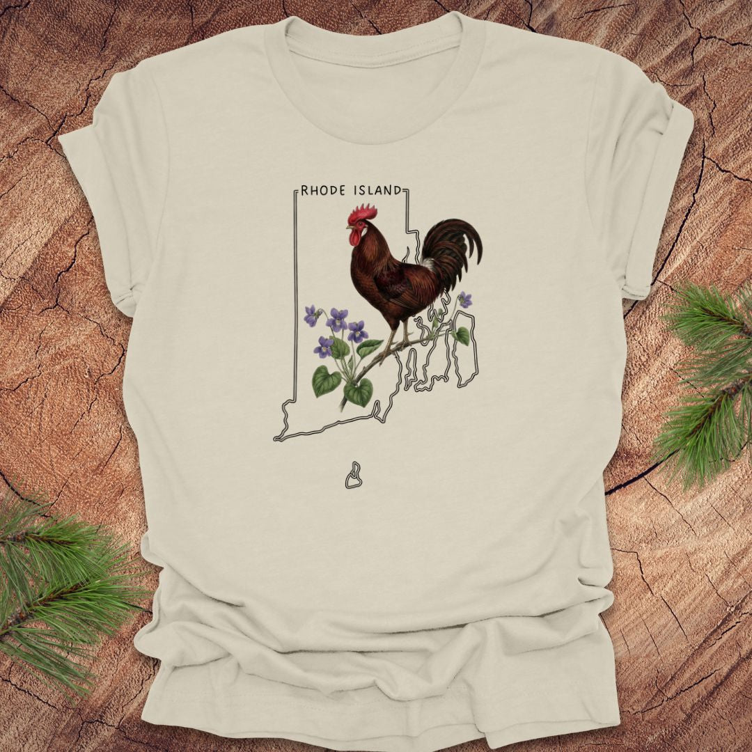 Beige t-shirt with the state outline of Rhode Island with state bird, red rooster and flower, violet,  on a wooden surface