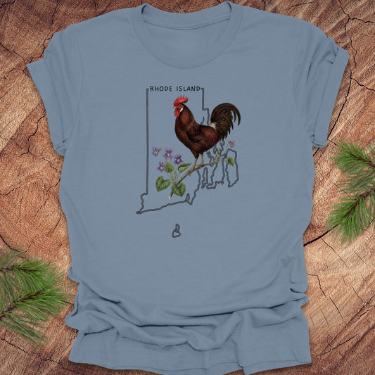 Steel blue t-shirt with the state outline of Rhode Island with state bird, red rooster and flower, violet,  on a wooden surface