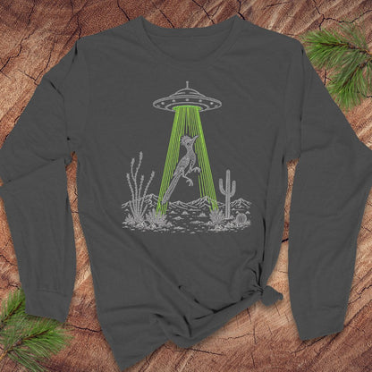 A gray long-sleeve t-shirt with a graphic of a bird under a UFO in a desert scene, laid flat on a rustic wood background with pine branches.