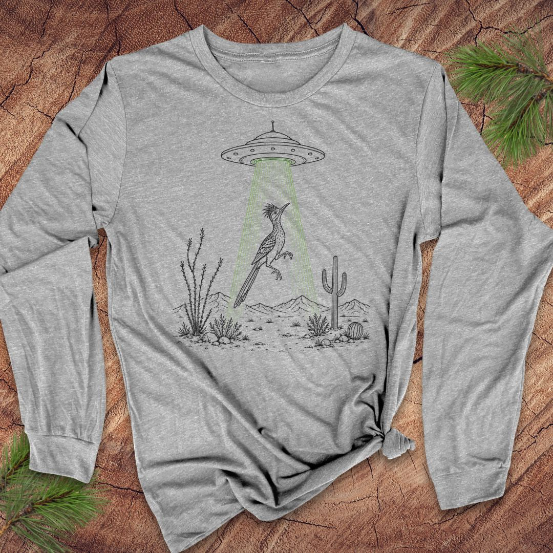 A heather gray long-sleeve t-shirt with a graphic of a bird under a UFO with green beam, styled flat on a wood background with pine branches.