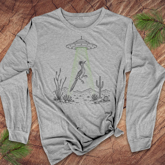 A heather gray long-sleeve t-shirt with a graphic of a bird under a UFO with green beam, styled flat on a wood background with pine branches.