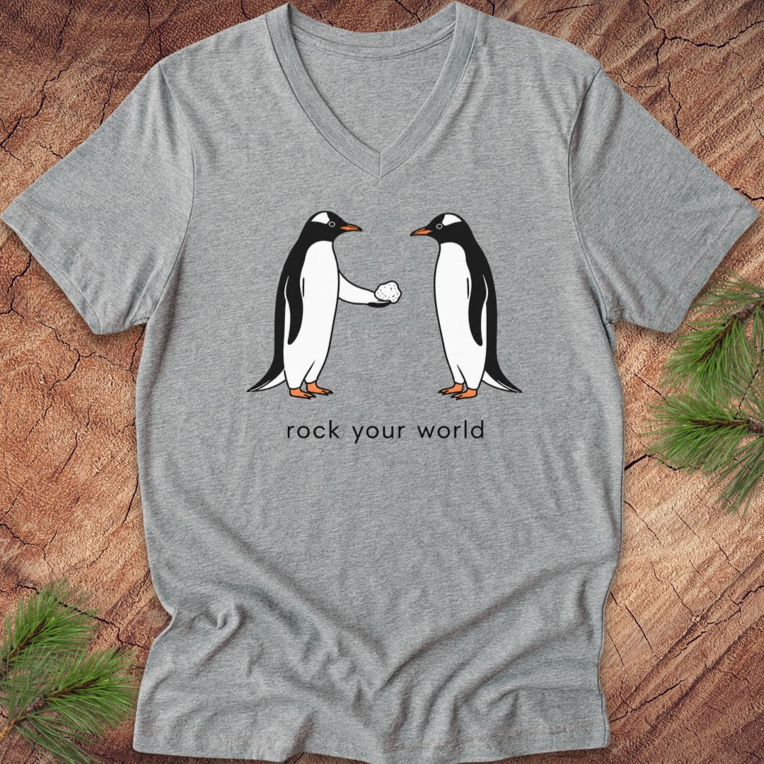 Gray v-neck t-shirt with two penguins and text, 'rock your world' on a wood background.