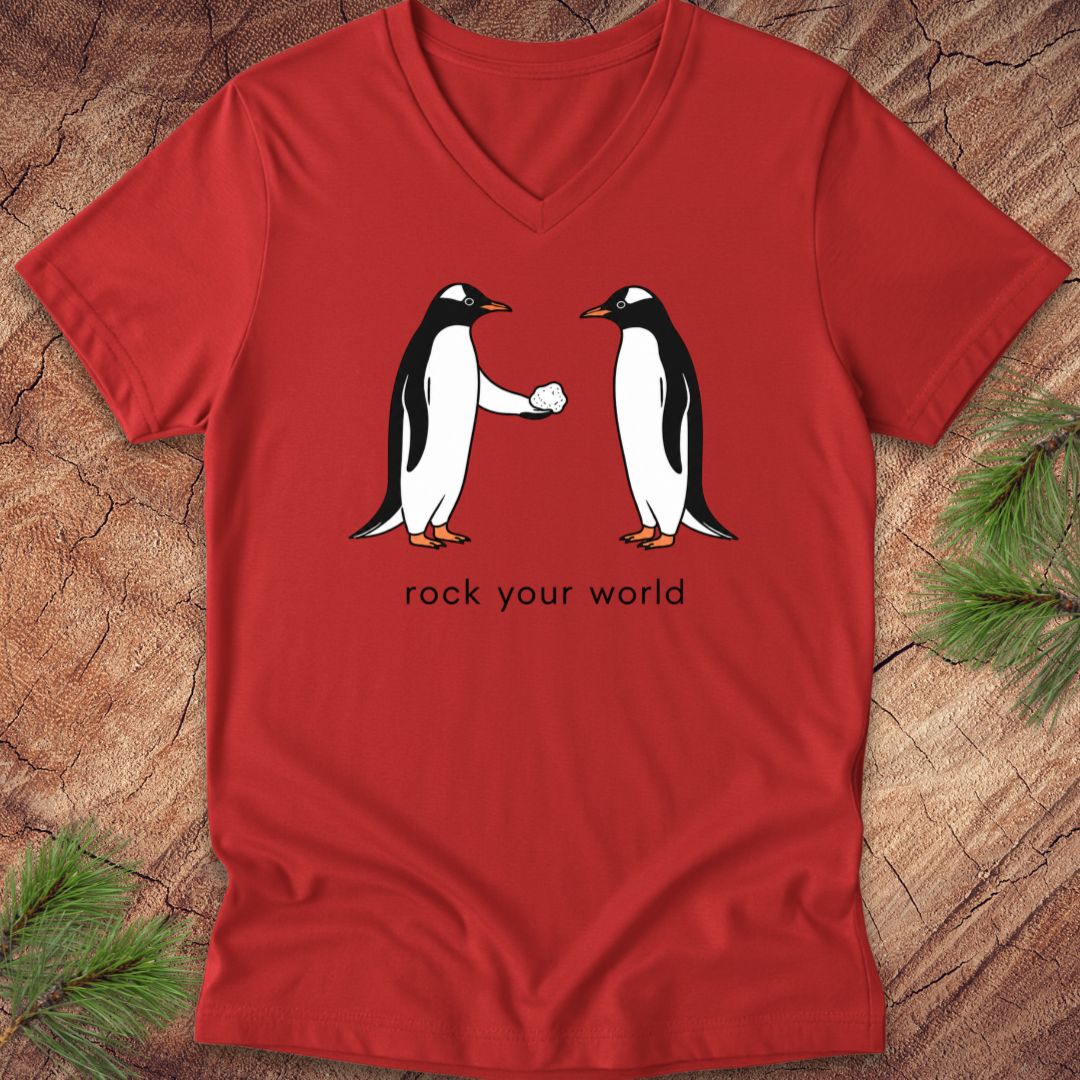 Red v-neck t-shirt with two penguins and text, 'rock your world' on a wood background.