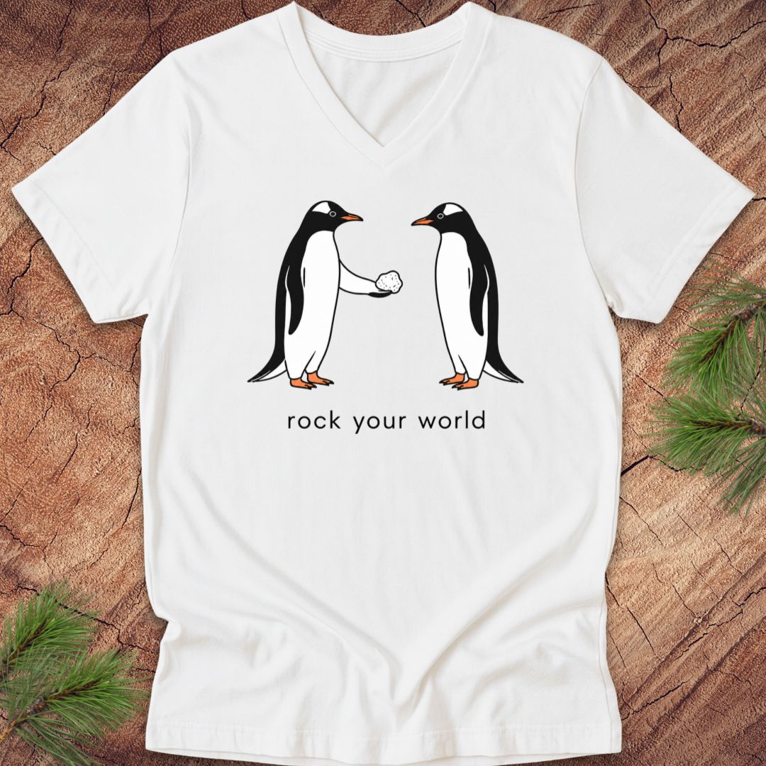 White v-neck t-shirt with two penguins and text, 'rock your world' on a wood background.