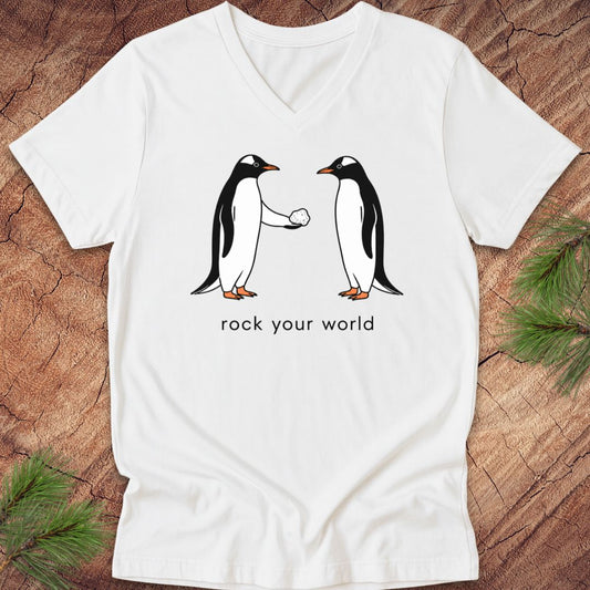 White v-neck t-shirt with two penguins and text, 'rock your world' on a wood background.