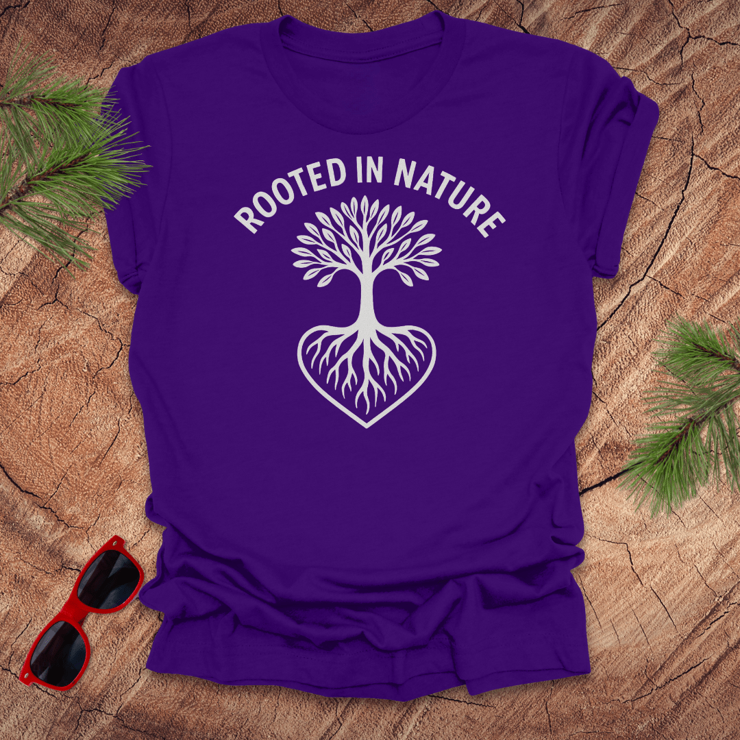 purple crew neck t-shirt with a white graphic of a tree with roots and the phrase 'ROOTED IN NATURE' printed above it, displayed on a wooden surface with pine needles and red sunglasses to the side.
