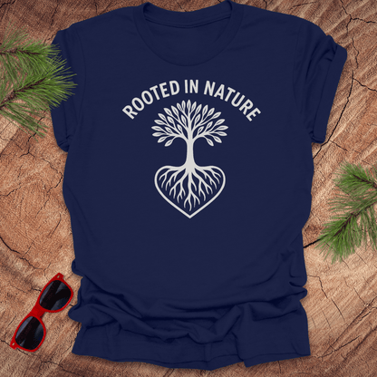 navy crew neck t-shirt with a white graphic of a tree with roots and the phrase 'ROOTED IN NATURE' printed above it, displayed on a wooden surface with pine needles and red sunglasses to the side.