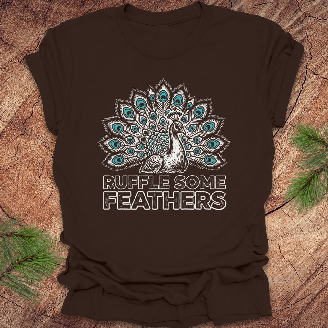 Brown t-shirt with peacock design and 'Ruffle Some Feathers' text on a wooden surface.