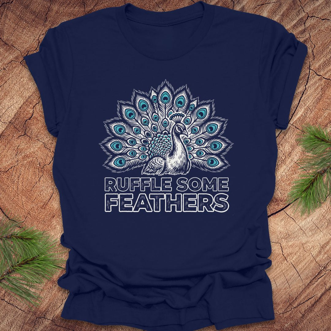 Navy blue t-shirt with peacock design and 'Ruffle Some Feathers' text on a wooden surface.