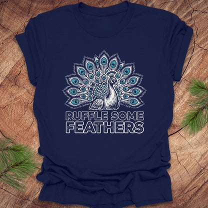 Navy blue t-shirt with peacock design and 'Ruffle Some Feathers' text on a wooden surface.