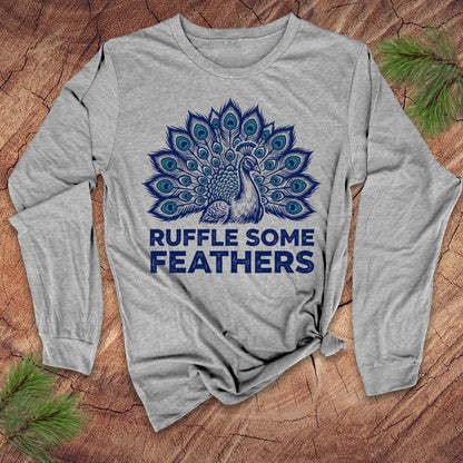 Gray long-sleeve shirt with peacock design and text 'Ruffle Some Feathers' on a wooden surface.