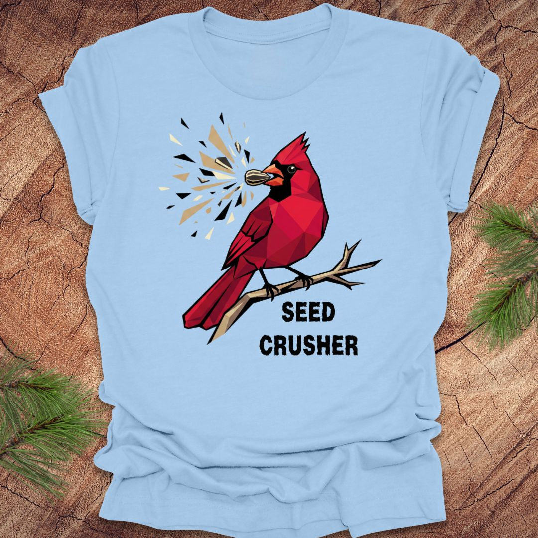 Light blue t-shirt with a red cardinal graphic and 'Seed Crusher' text on a wooden surface.