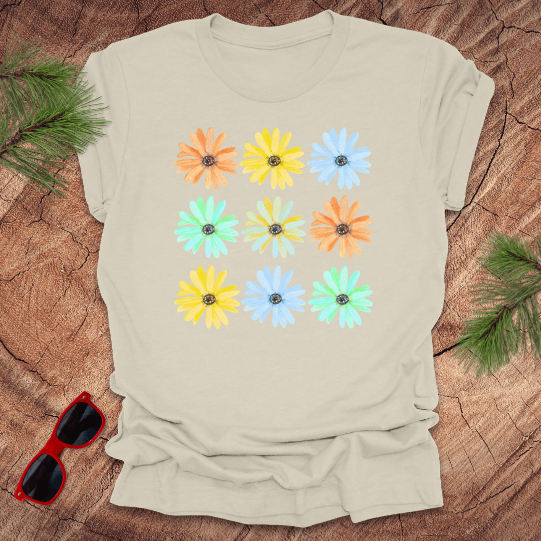 Beige t-shirt with colorful flower pattern on a wooden surface with sunglasses and greenery.