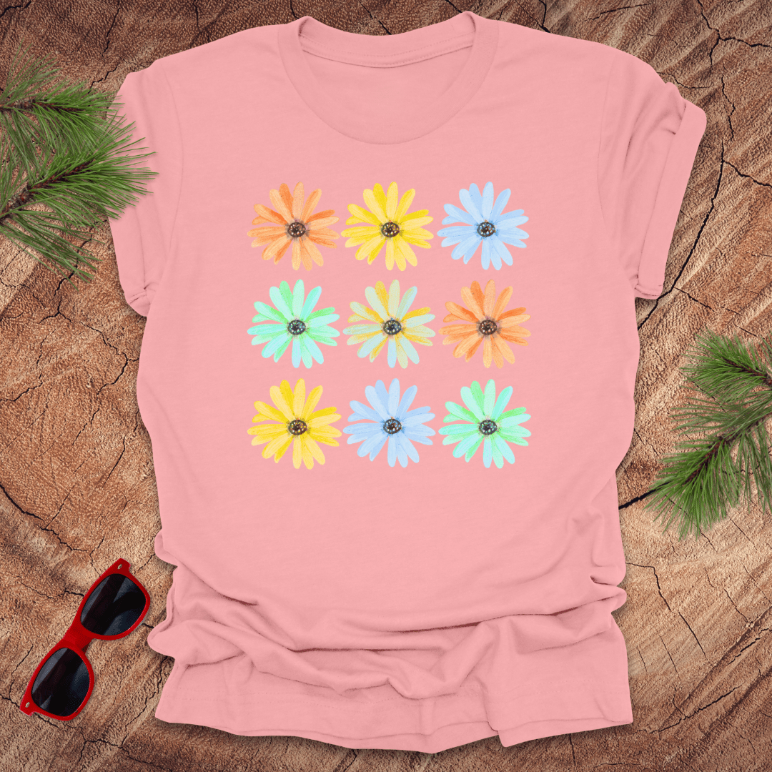 Pink t-shirt with colorful flower pattern on a wooden surface with sunglasses and greenery.
