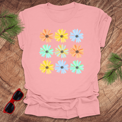 Pink t-shirt with colorful flower pattern on a wooden surface with sunglasses and greenery.