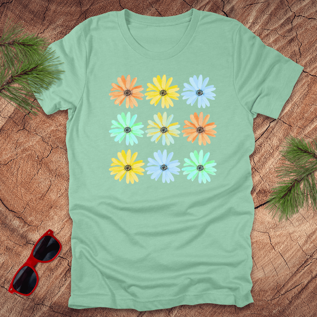 Light green t-shirt with colorful flower pattern on a wooden surface with sunglasses and leaves.