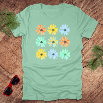 Light green t-shirt with colorful flower pattern on a wooden surface with sunglasses and leaves.