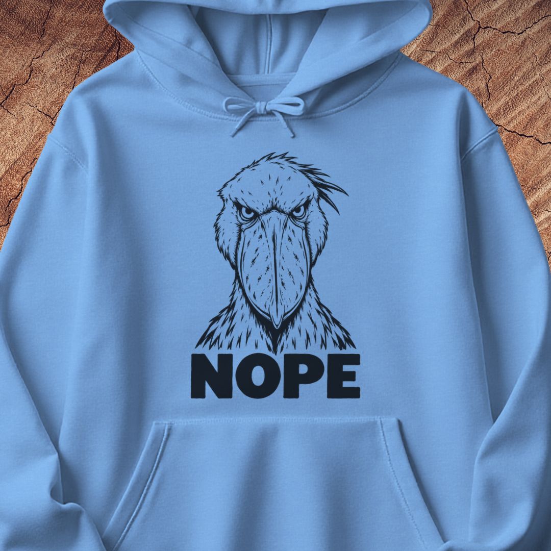Carolina blue hoodie with a black line-art Shoebill staring straight ahead above the word NOPE, laid flat on a rustic wood background.