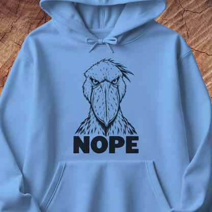Carolina blue hoodie with a black line-art Shoebill staring straight ahead above the word NOPE, laid flat on a rustic wood background.