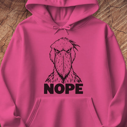 Heliconia pink hoodie with a black line-art Shoebill staring straight ahead above the word NOPE, laid flat on a rustic wood background.