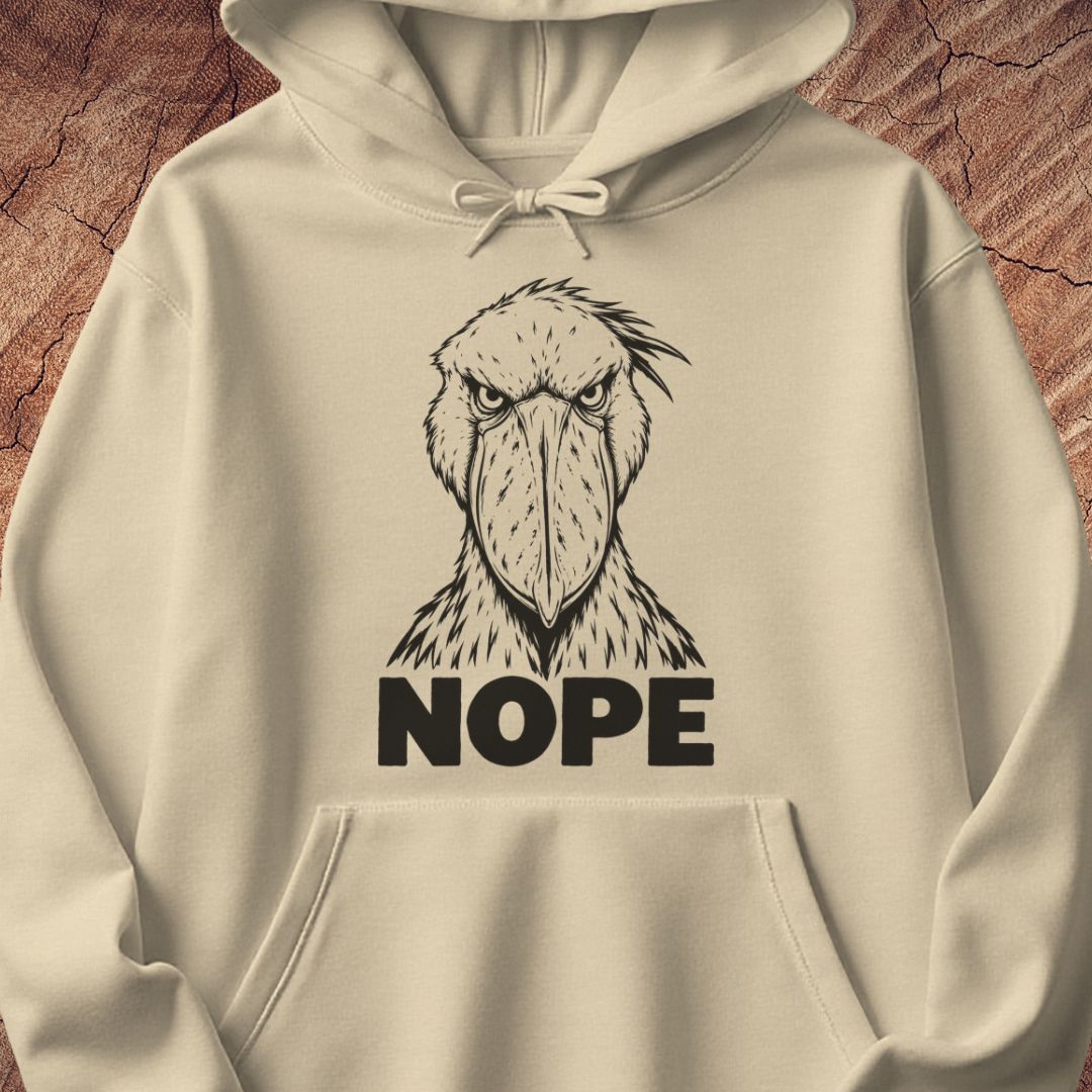 Sand beige hoodie with a black line-art Shoebill staring straight ahead above the word NOPE, laid flat on a rustic wood background.