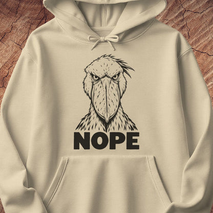 Sand beige hoodie with a black line-art Shoebill staring straight ahead above the word NOPE, laid flat on a rustic wood background.