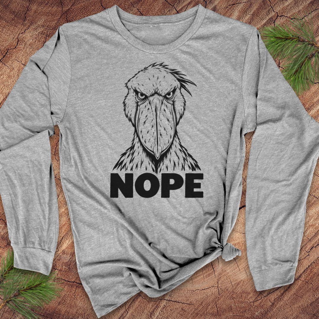 Athletic heather gray long-sleeve t-shirt with a black line-art Shoebill staring straight ahead above the word NOPE, laid flat on a rustic wood background with pine branches.