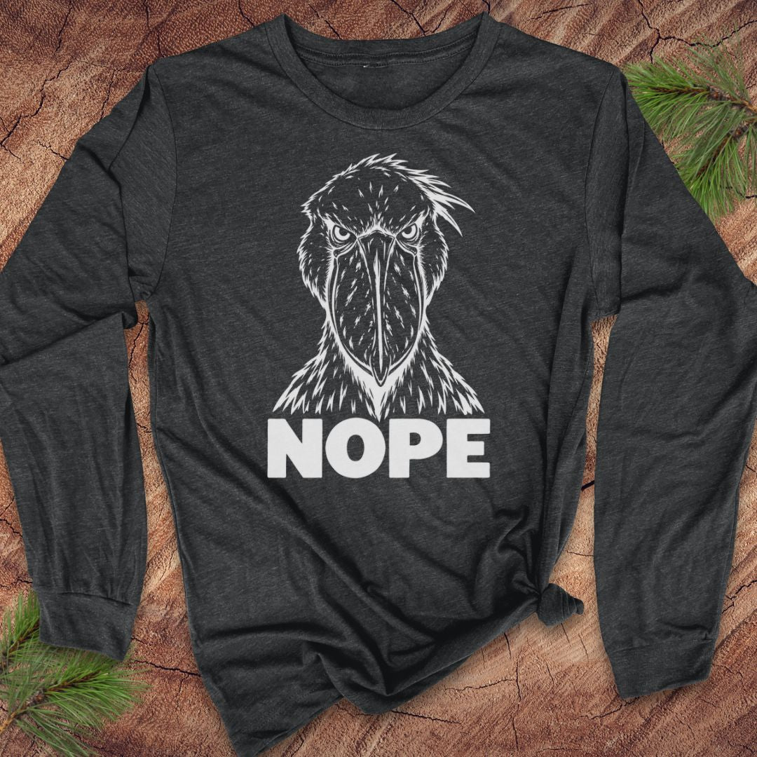 Dark grey heather long-sleeve t-shirt with a white line-art Shoebill staring straight ahead above the word NOPE, laid flat on a rustic wood background with pine branches.