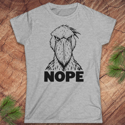 Sport grey women's t-shirt with a black line-art Shoebill staring straight ahead above the word NOPE, laid flat on a rustic wood background with pine branches.