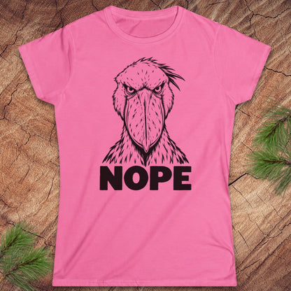 Azalea pink women's t-shirt with a black line-art Shoebill staring straight ahead above the word NOPE, laid flat on a rustic wood background with pine branches.