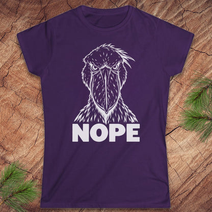 Purple women's t-shirt with a white line-art Shoebill staring straight ahead above the word NOPE, laid flat on a rustic wood background with pine branches.